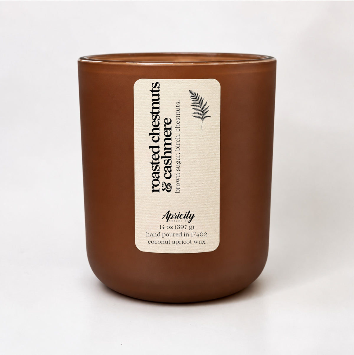 Roasted Chestnuts & Cashmere 14 oz candle in a frosted chocolate brown tumbler with a cream fern label reading brown sugar, birch, chestnuts