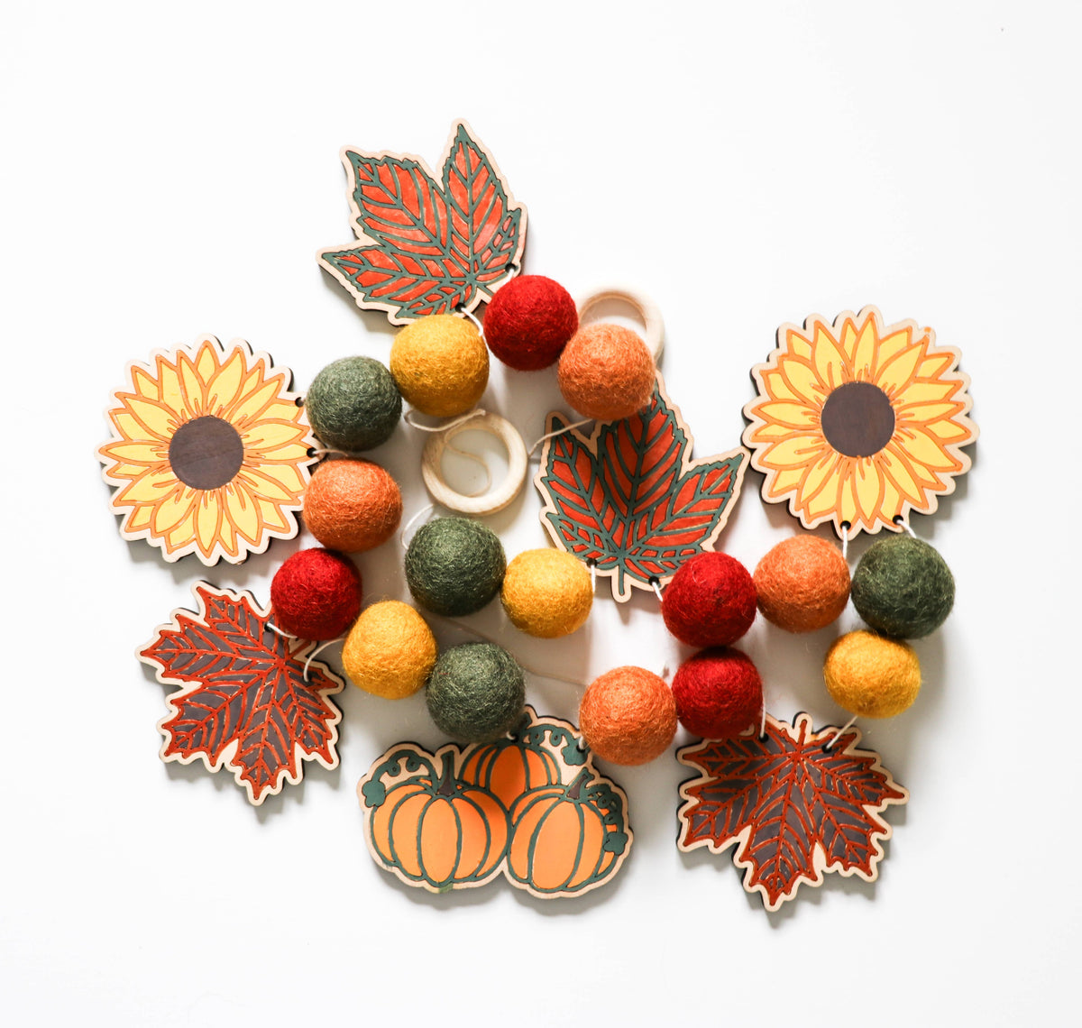 Painted wooden sunflower, leaf and pumpkin cutouts with fall felt balls for a DIY garland