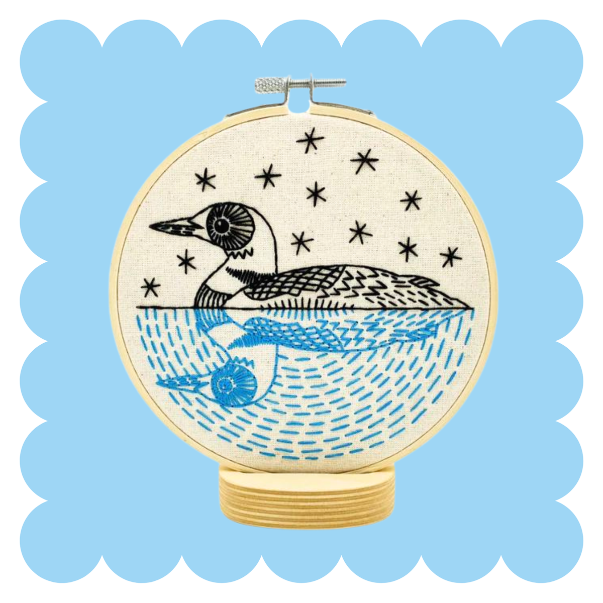 Embroidery hoop with stitched loon on a lake under a starry sky in blue and black