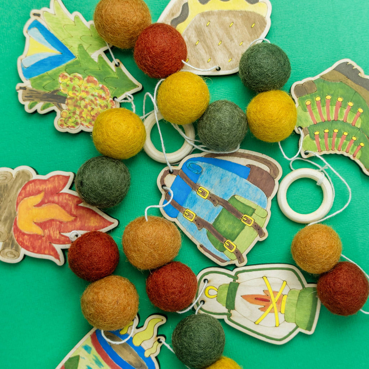 Painted wooden tent, campfire and lantern cutouts with felt balls for a DIY garland