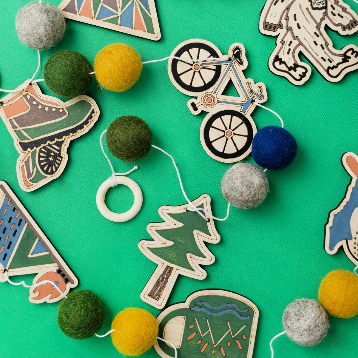 Painted wooden Sasquatch, tree, canoe and tent cutouts with felt balls for a DIY garland