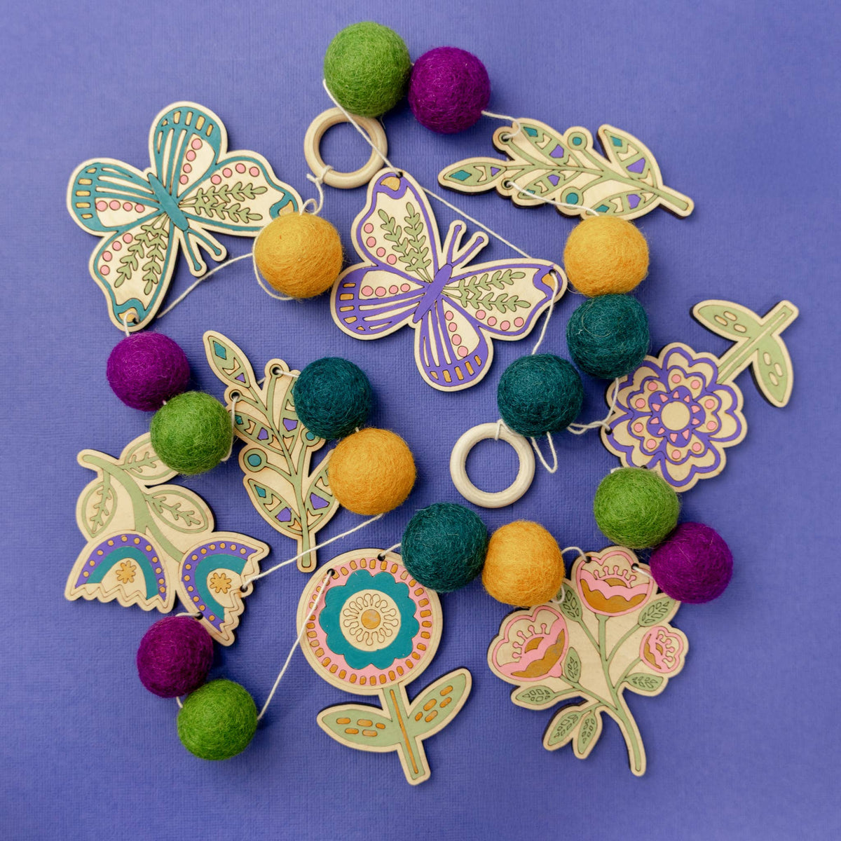 Painted wooden folk art flower and butterfly cutouts with felt balls for a DIY garland
