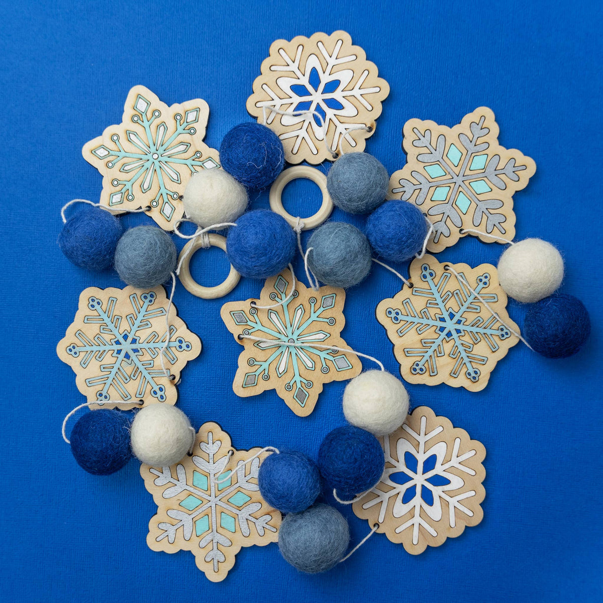 Painted wooden snowflake cutouts and blue and white felt balls for a DIY garland